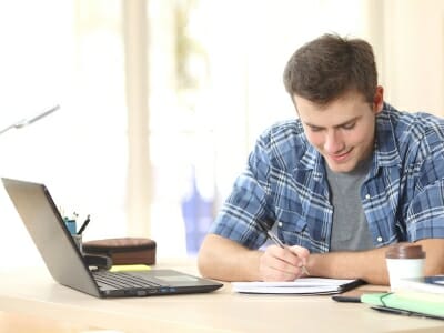 Boy taking notes whilst working with online tutor